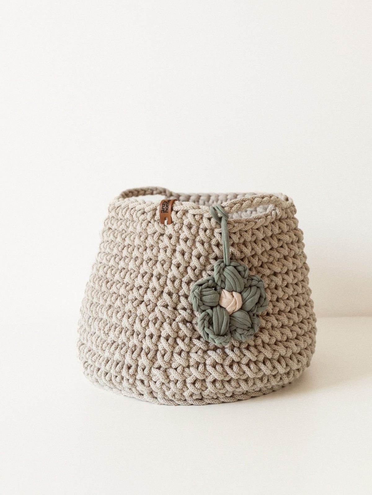 Cream crochet storage basket with muted green braided flower and side handles