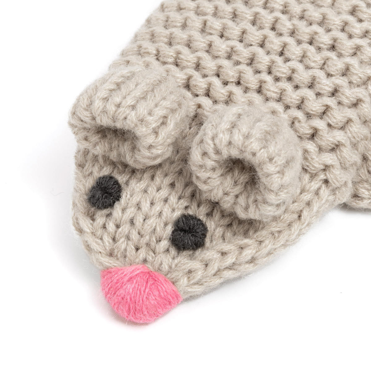 Close-up of a beige knit mitten's mouse face with black eyes and a pink nose