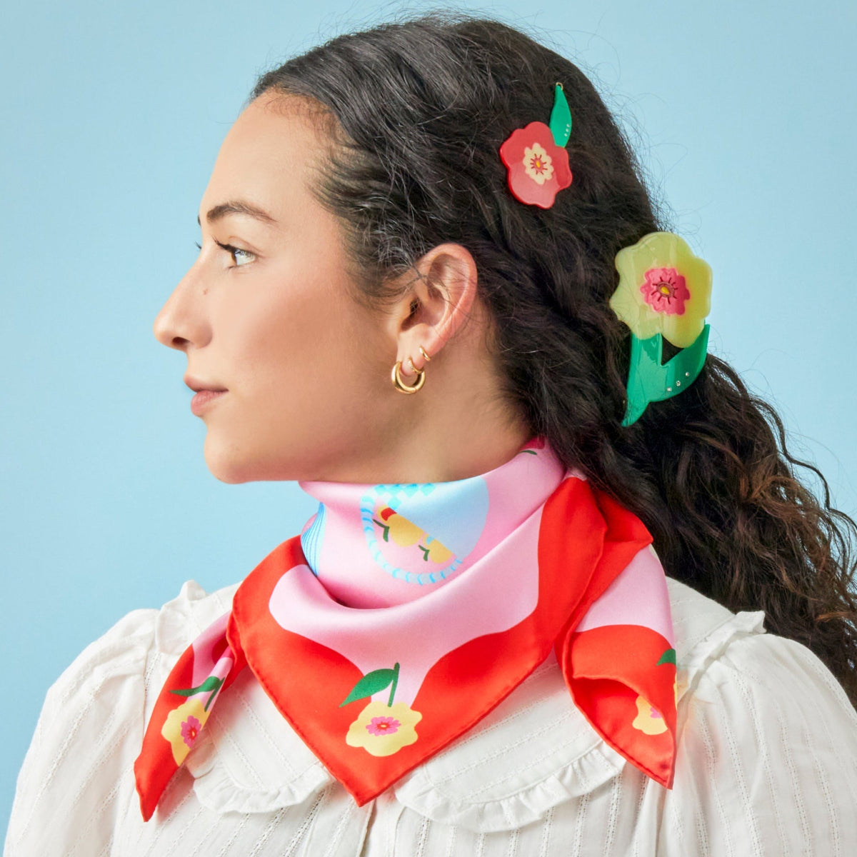 Silk square scarf tied at neck, red and pink with cats, flowers, and fruit pattern