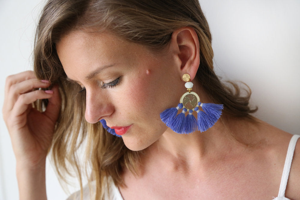 Blue tassel drop earrings worn on ear with gold disc and white bead detail