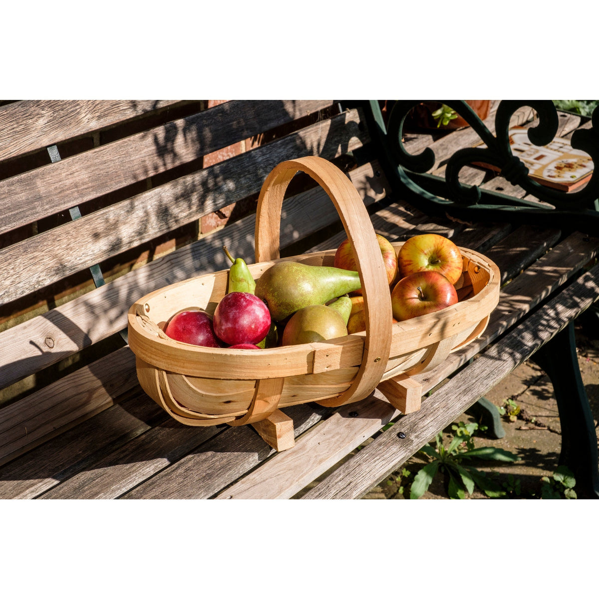 Natural wooden trug with arched handle, filled with mixed apples on a bench