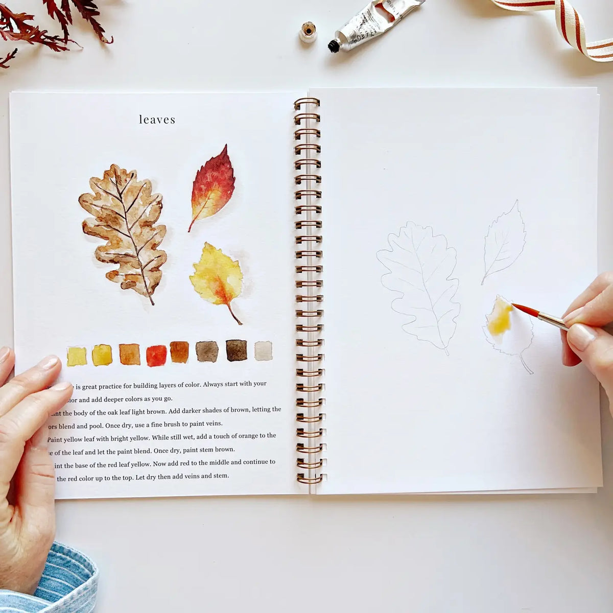 Open watercolor workbook spread with painted leaves, color swatches, and paintbrush
