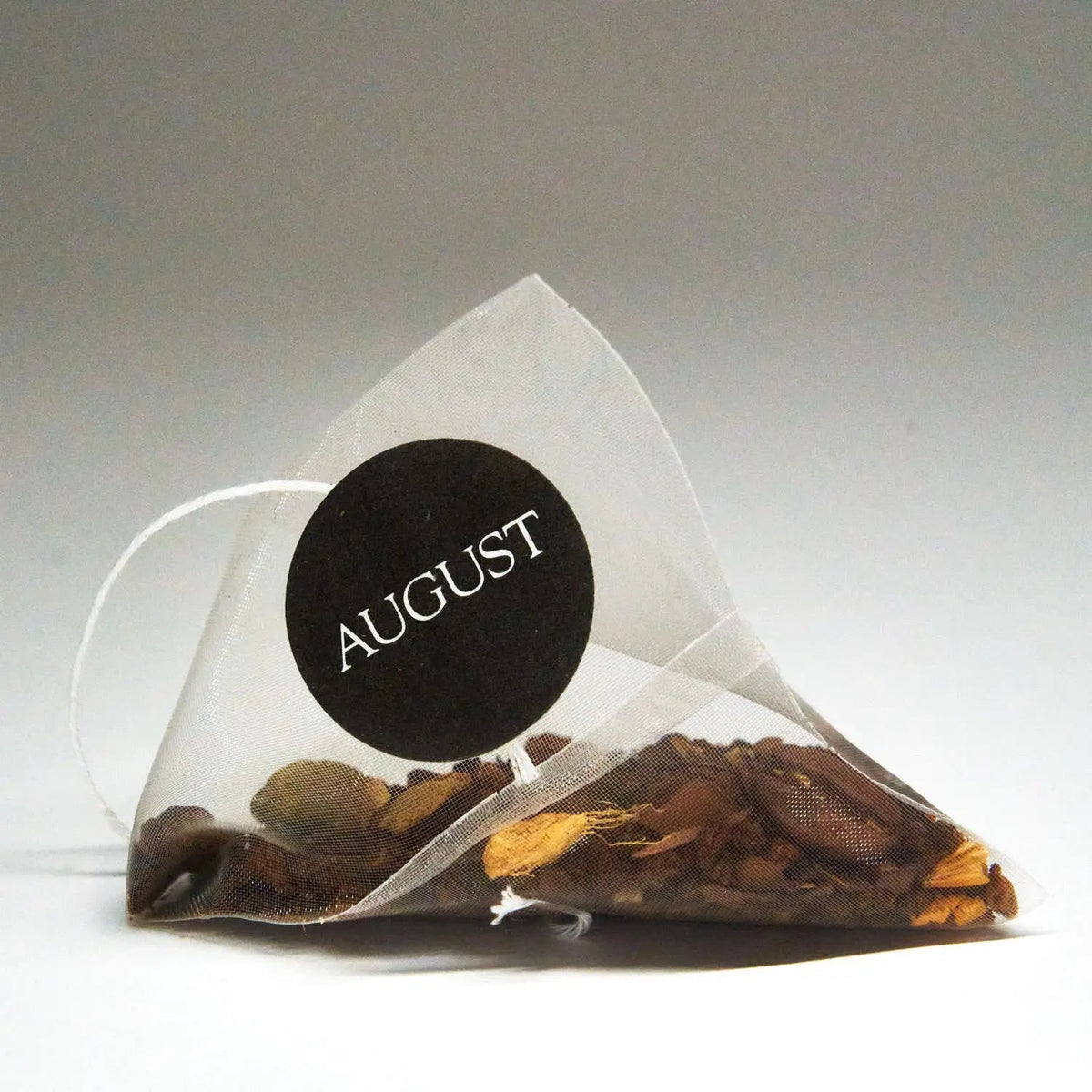 Pyramid tea bag filled with Dirty Chai tea leaves and spices, with an AUGUST tag.