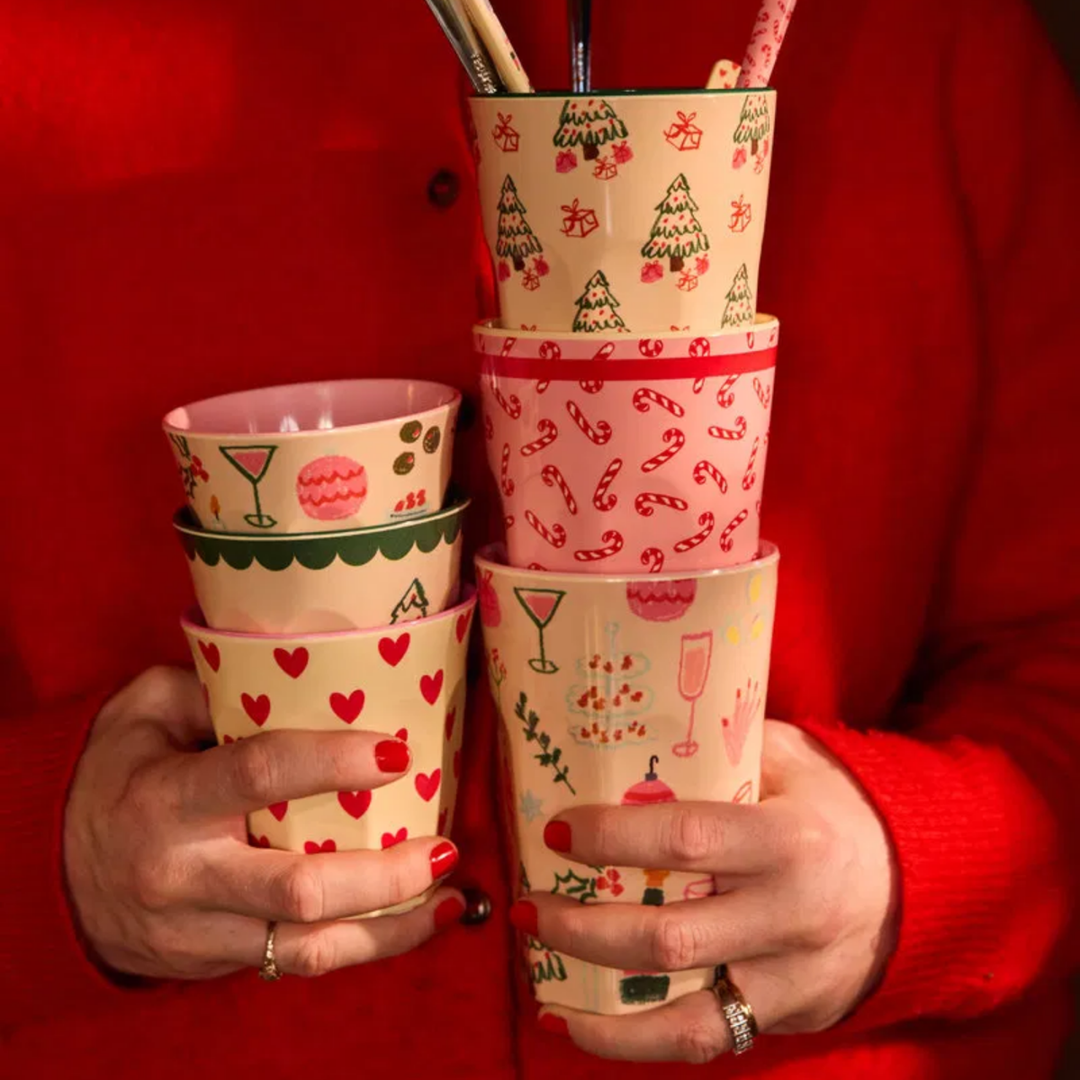 Tall melamine cups set, pink with red holiday prints, held in hands
