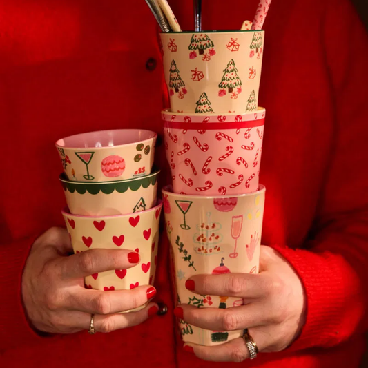 Tall melamine cups set, pink with red holiday prints, held in hands