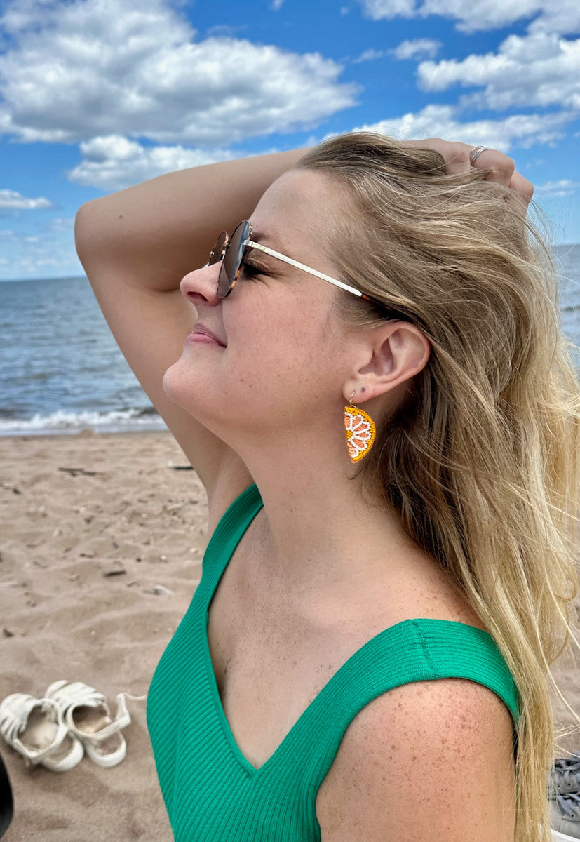 Citrus-slice beaded drop earrings on model, orange and white with gold hooks