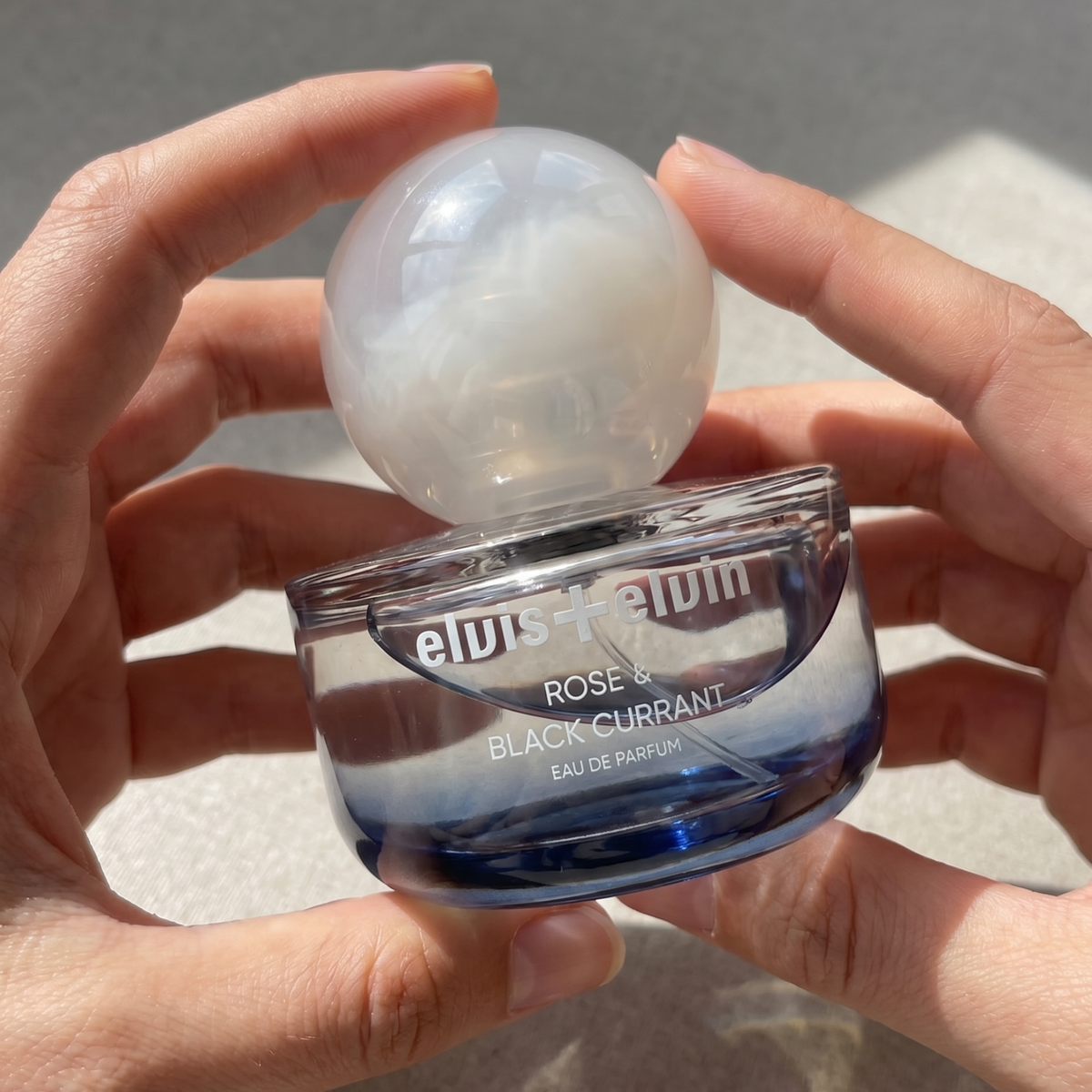 Rose & Black Currant Eau de Parfum jar held in hands with frosted globe cap