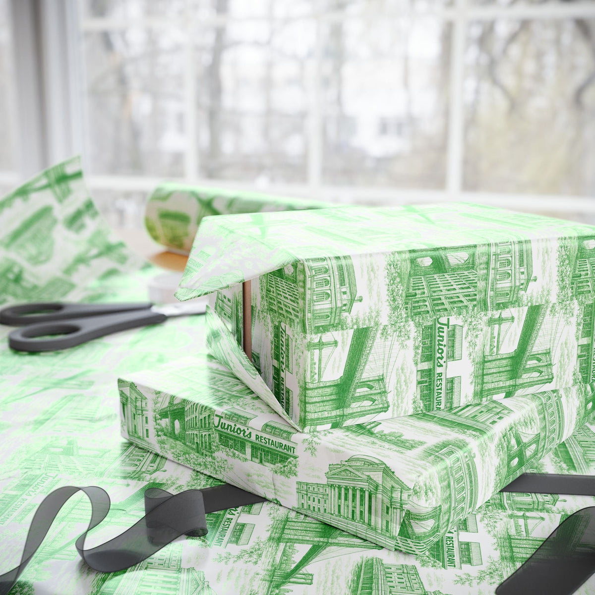 Green glossy gift wrap rolls on a table with city building toile print and ribbon