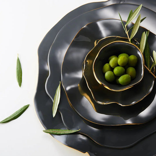 Graphite ruffled ceramic serving plate with gold-edged rim, holding green olives