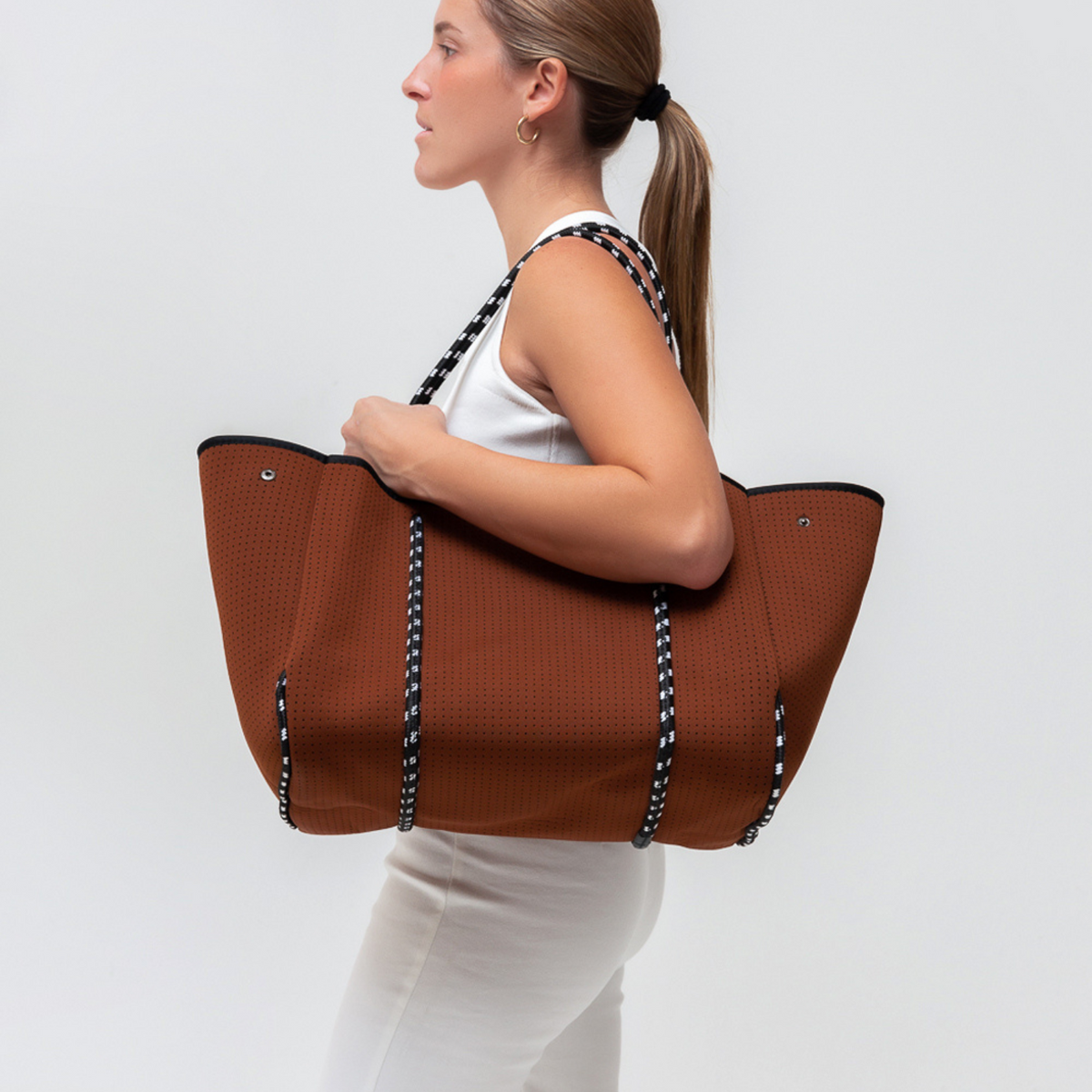 Rust-brown perforated tote with black handles and inner pocket, carried by person