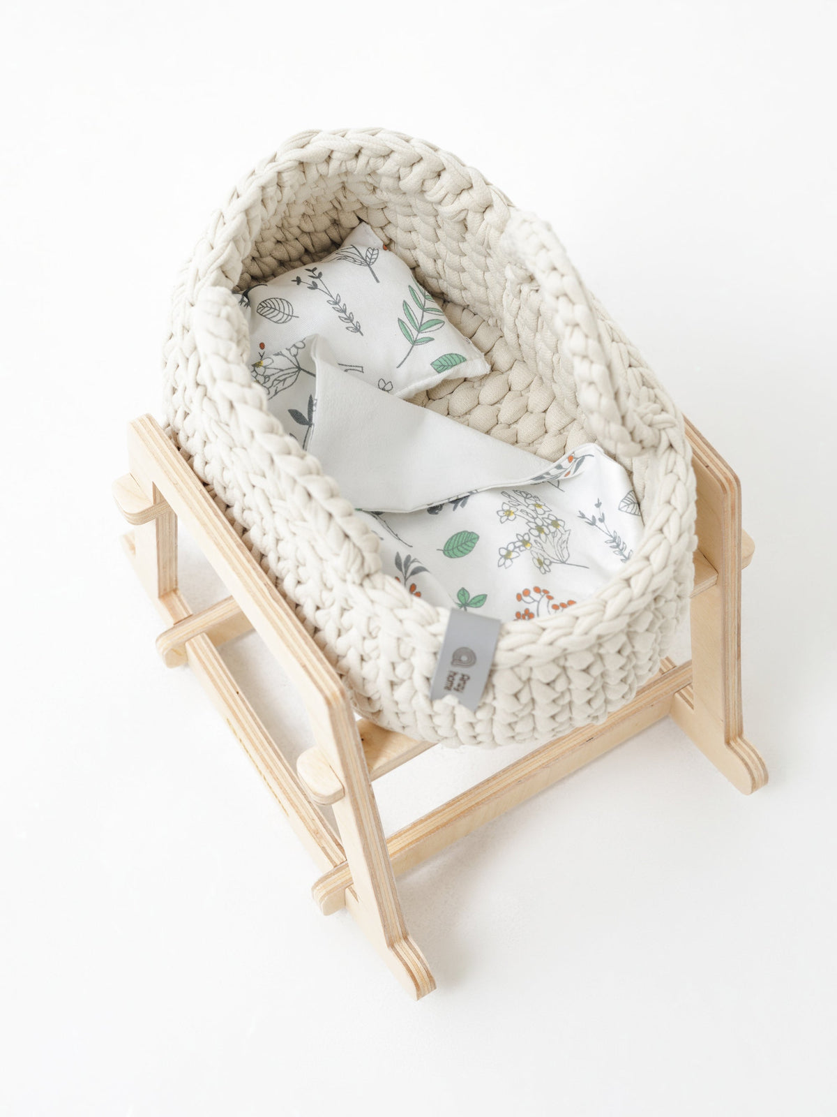 Cream woven moses basket on light wood rocking stand, patterned bedding inside