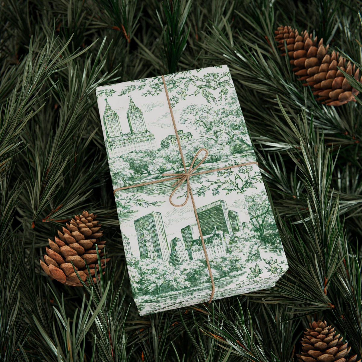 Green and white toile gift wrap with city buildings, trees, and brown ribbon tie