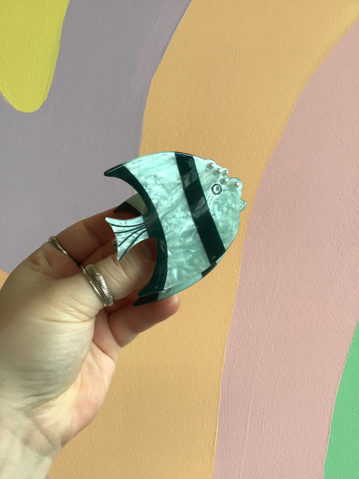 Green and teal fish-shaped hair claw with black stripe and metallic shine
