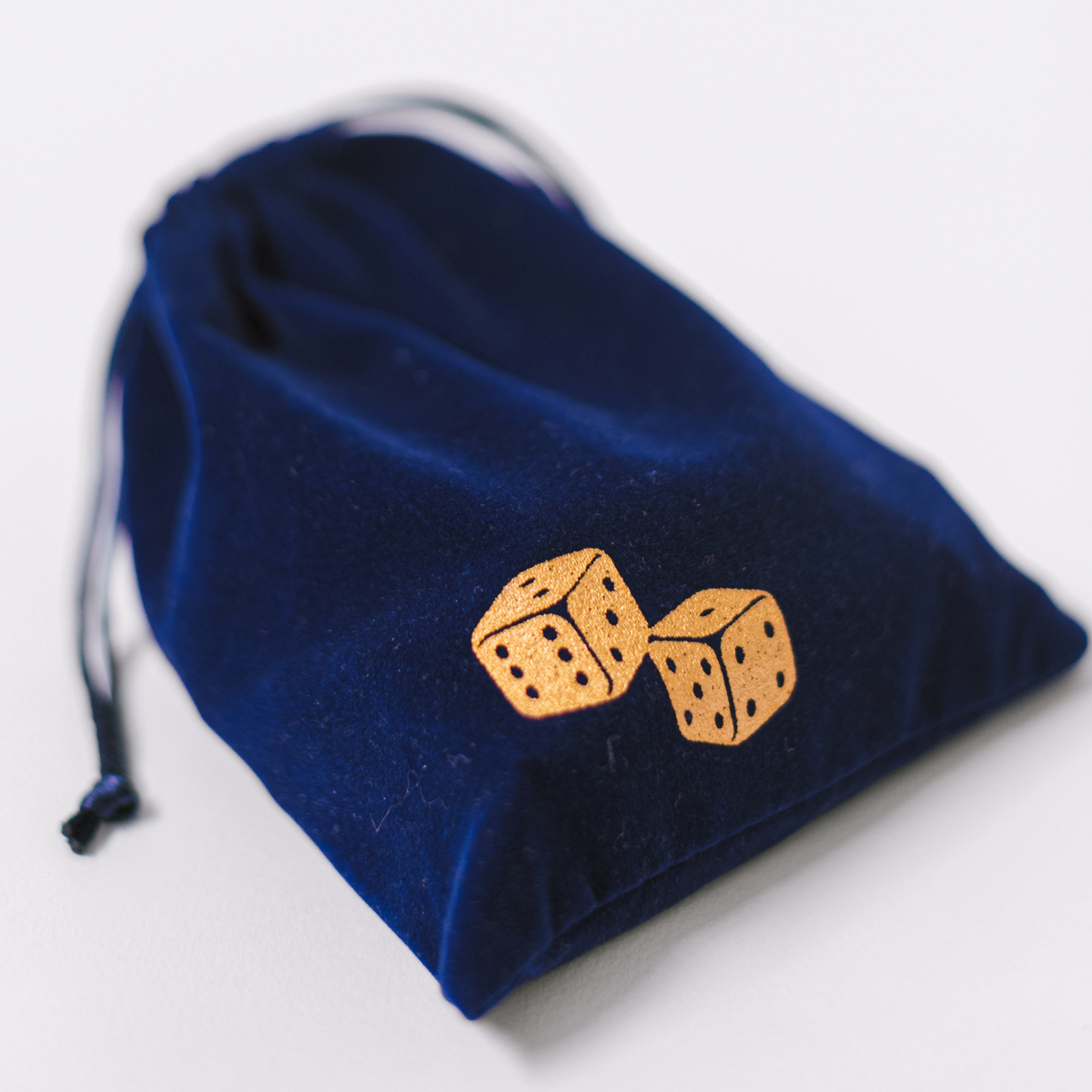 Navy velvet drawstring pouch with embroidered dice motif and three dice graphic.