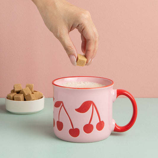 Pink ceramic mug with red cherry pattern, red handle and rim, filled with foam