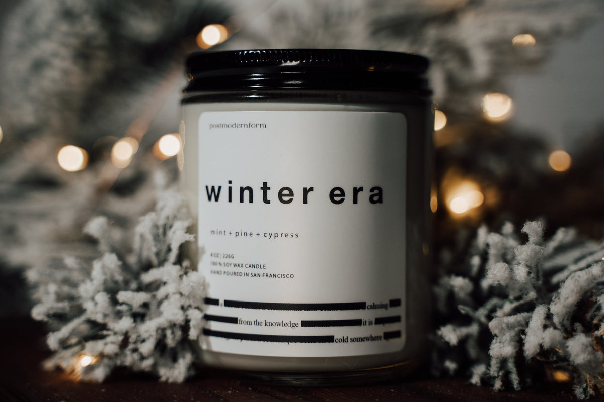 Scented candle jar with black lid on pine-like base and 'winter era' label