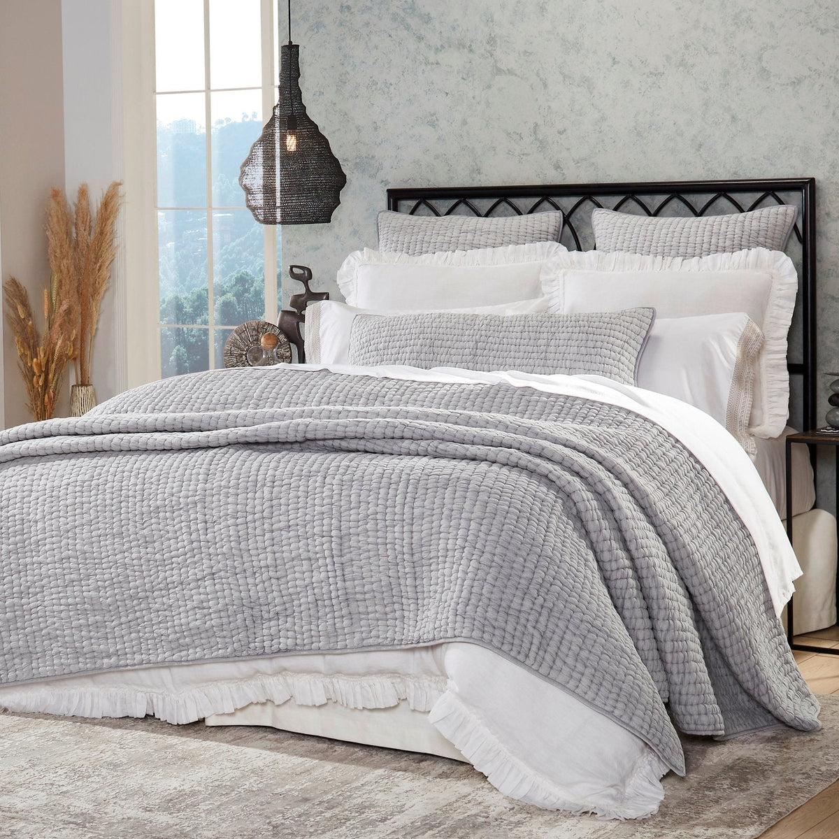 Gray stone-washed cotton quilt with textured weave, layered on bed with pillows.