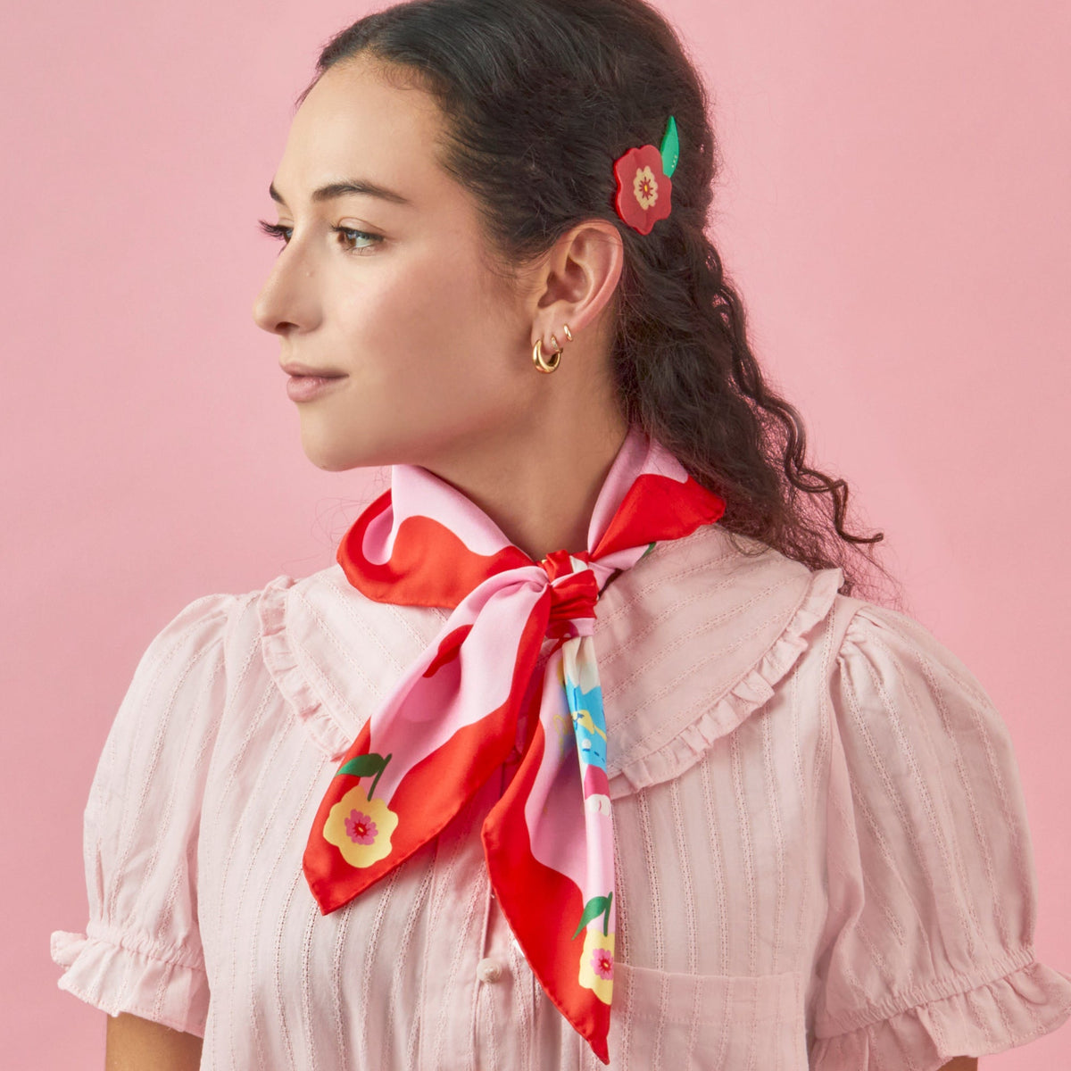 Silk square scarf tied at neck, red and pink with colorful fruit and flower print