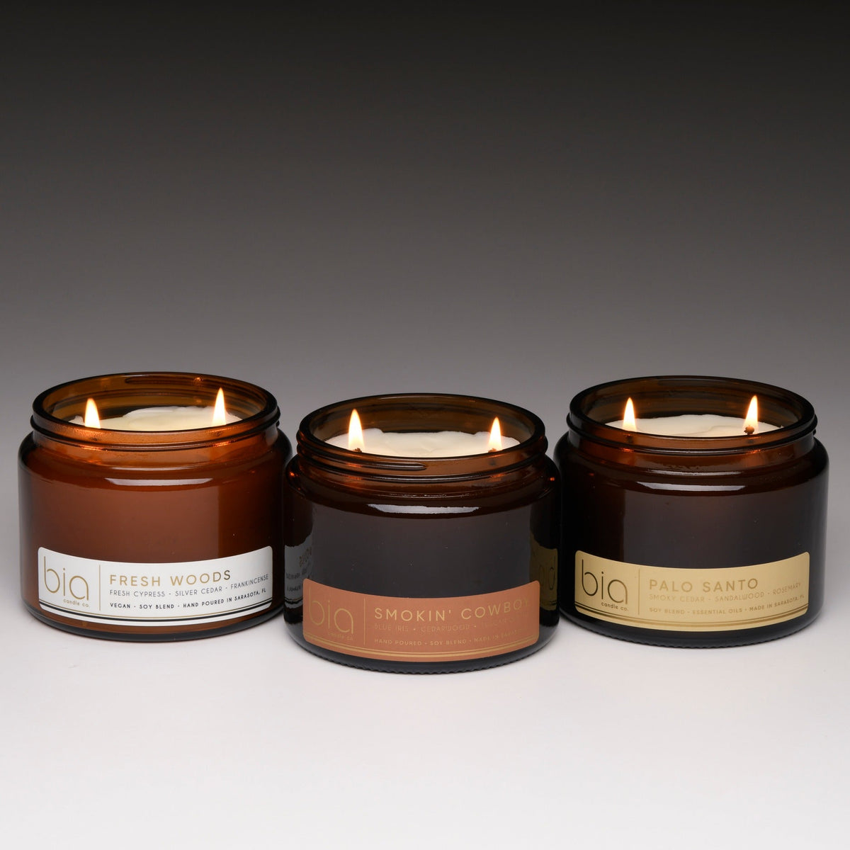 Set of three amber glass soy candles with labels and wicks, all lit