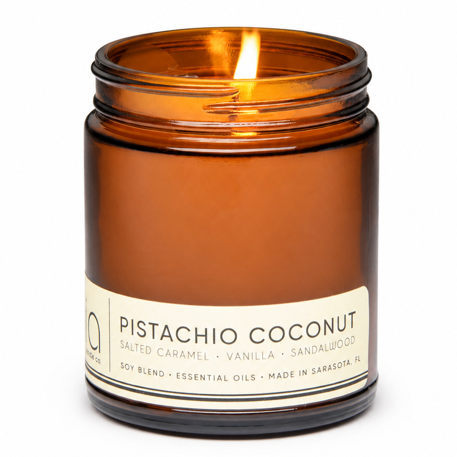 Close-up of lit amber glass jar candle with cream label and flame