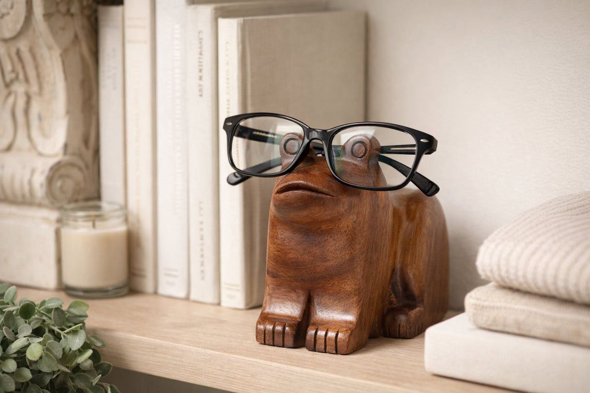 Wooden frog eyeglass holder stand with black-framed eyeglasses resting on top