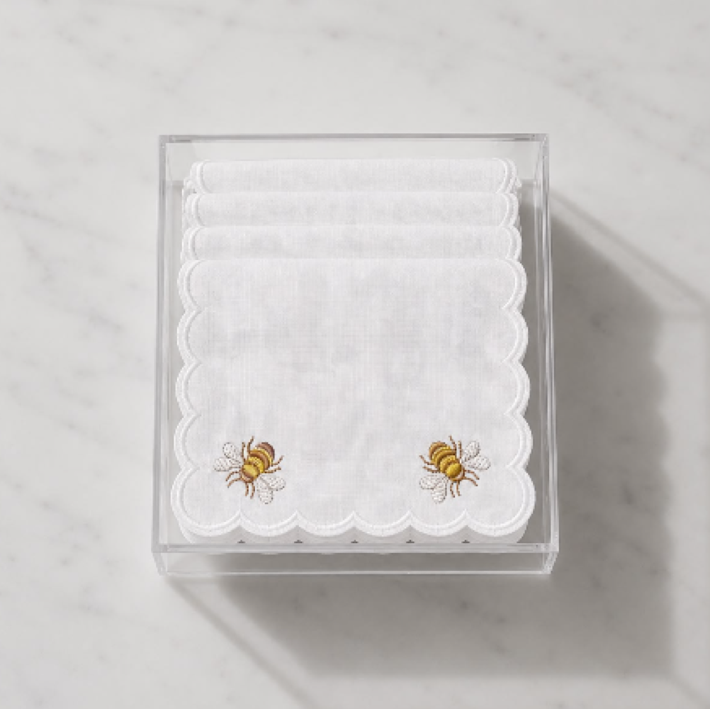 Stack of white cocktail napkins in clear box, scalloped edges, embroidered honey bees