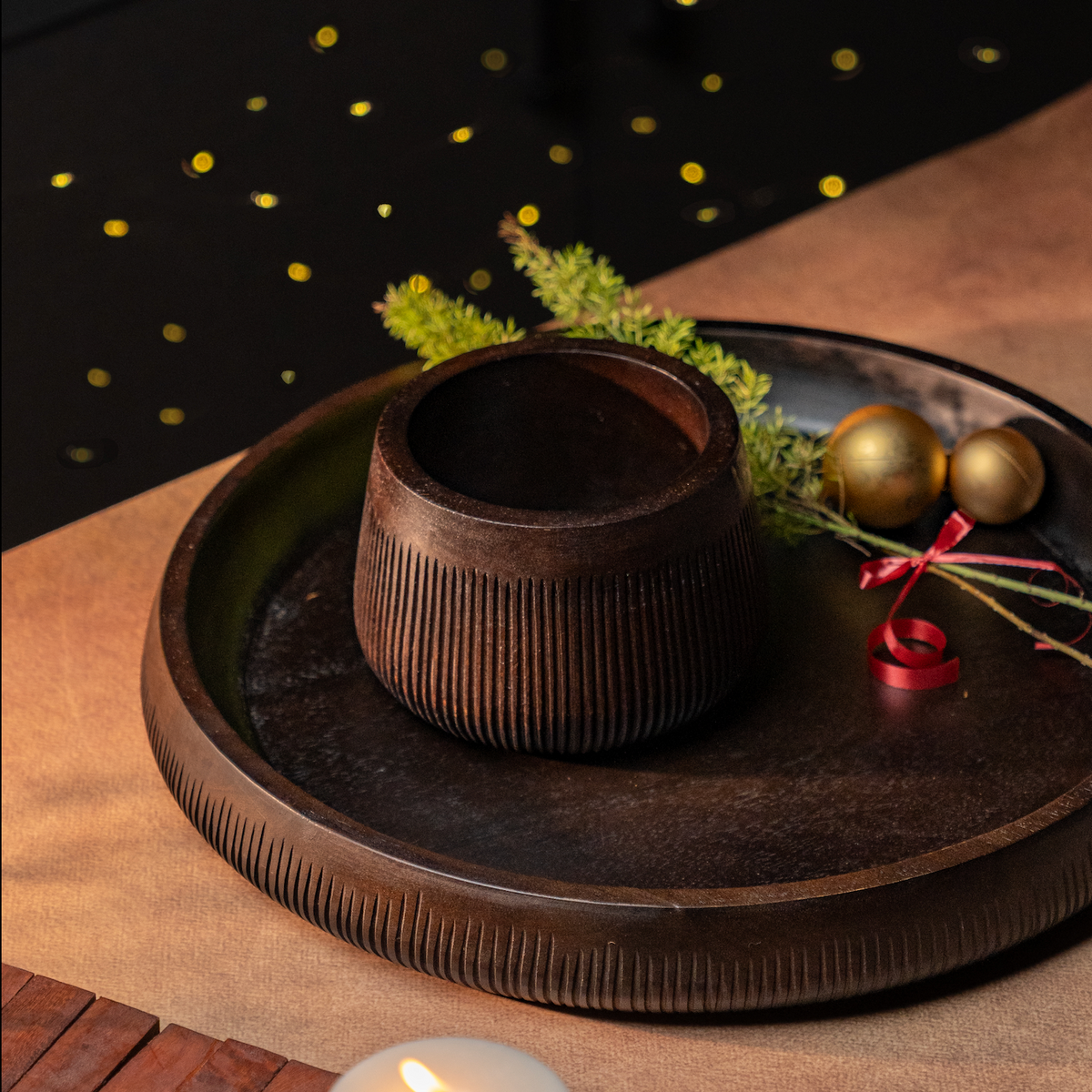 Dark ridged ceramic bowl centered on a round tray with gift accents