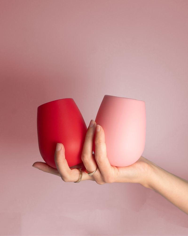 Hands holding cherry red and blush pink silicone tulip glasses, unbreakable style