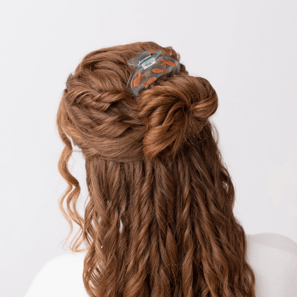 Fish hair claw clip holding brown hair, clear blue shell with orange goldfish details