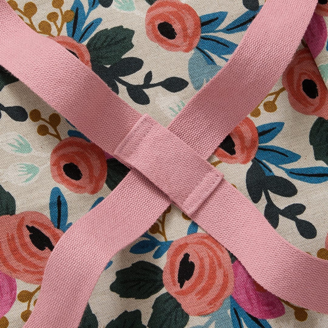 Floral crossback apron cross-strap detail with reinforced seam and pink webbing.