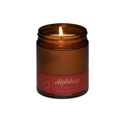 Amber glass soy candle jar with lid and lit wick, “Holidays” label on front