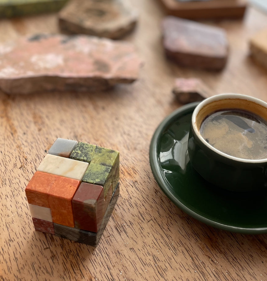 Gemstone cube puzzle with green, orange, and cream blocks beside a cup on a tray.