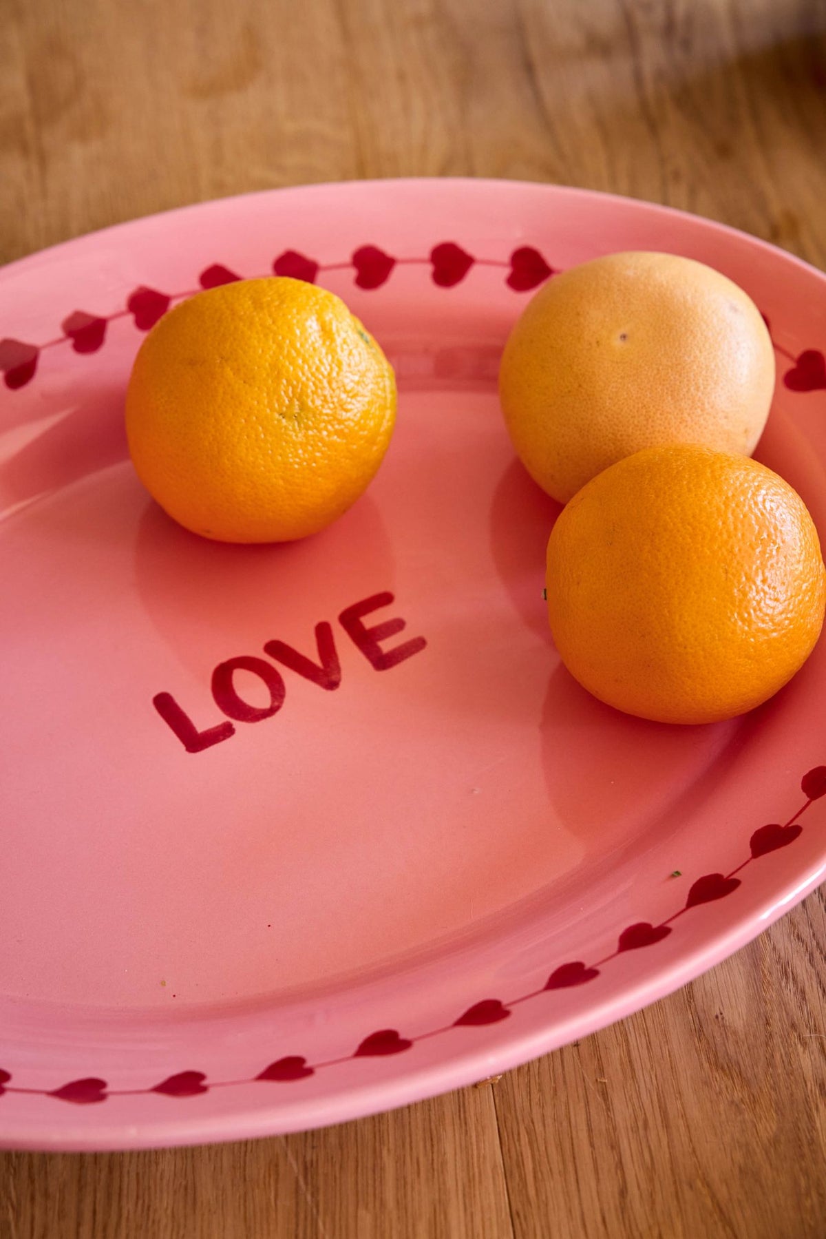 Pink ceramic serving platter with red hearts, LOVE text, and three orange fruits