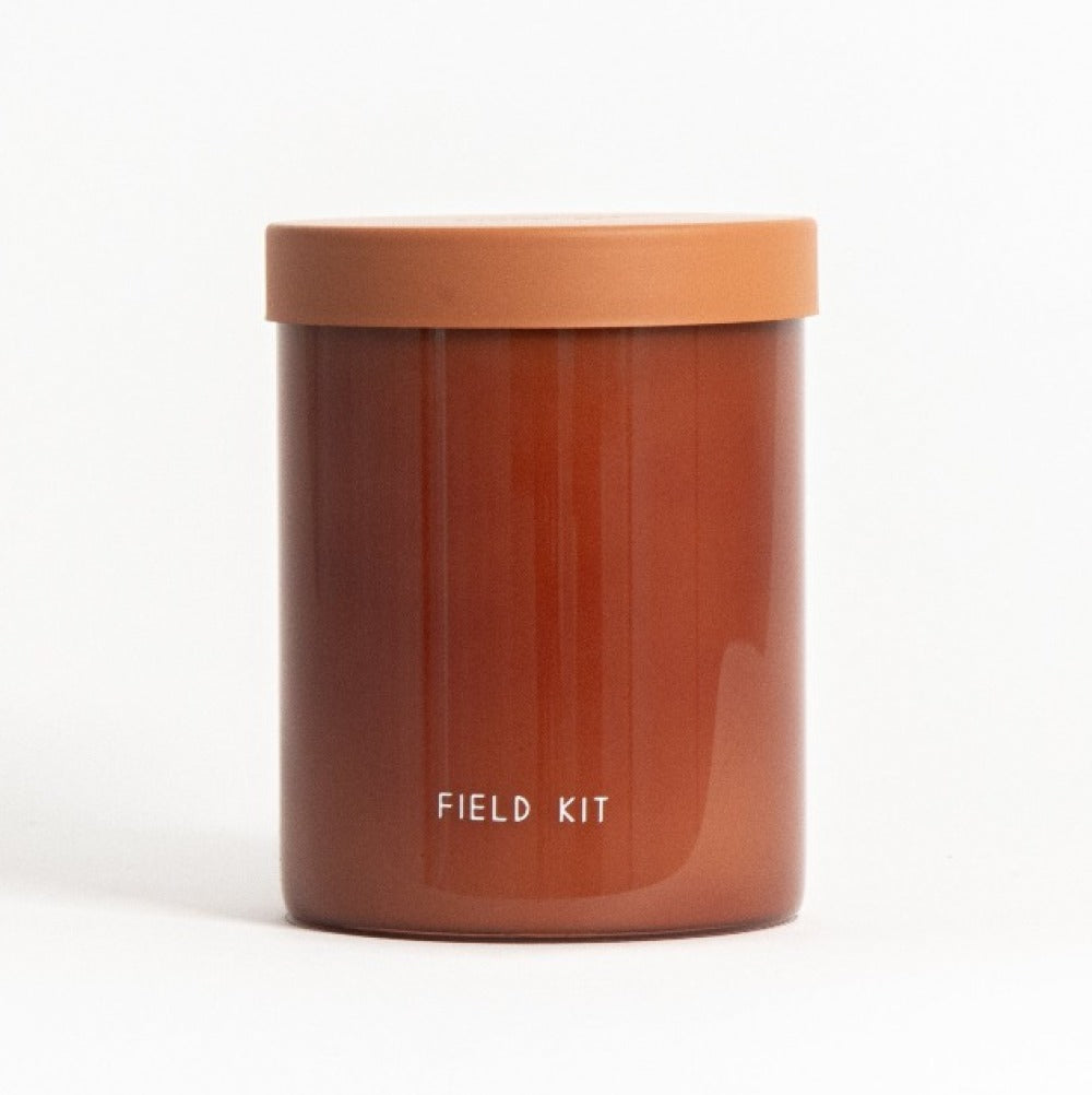 Scented candle in amber glass jar with orange lid, label reading FIELD KIT