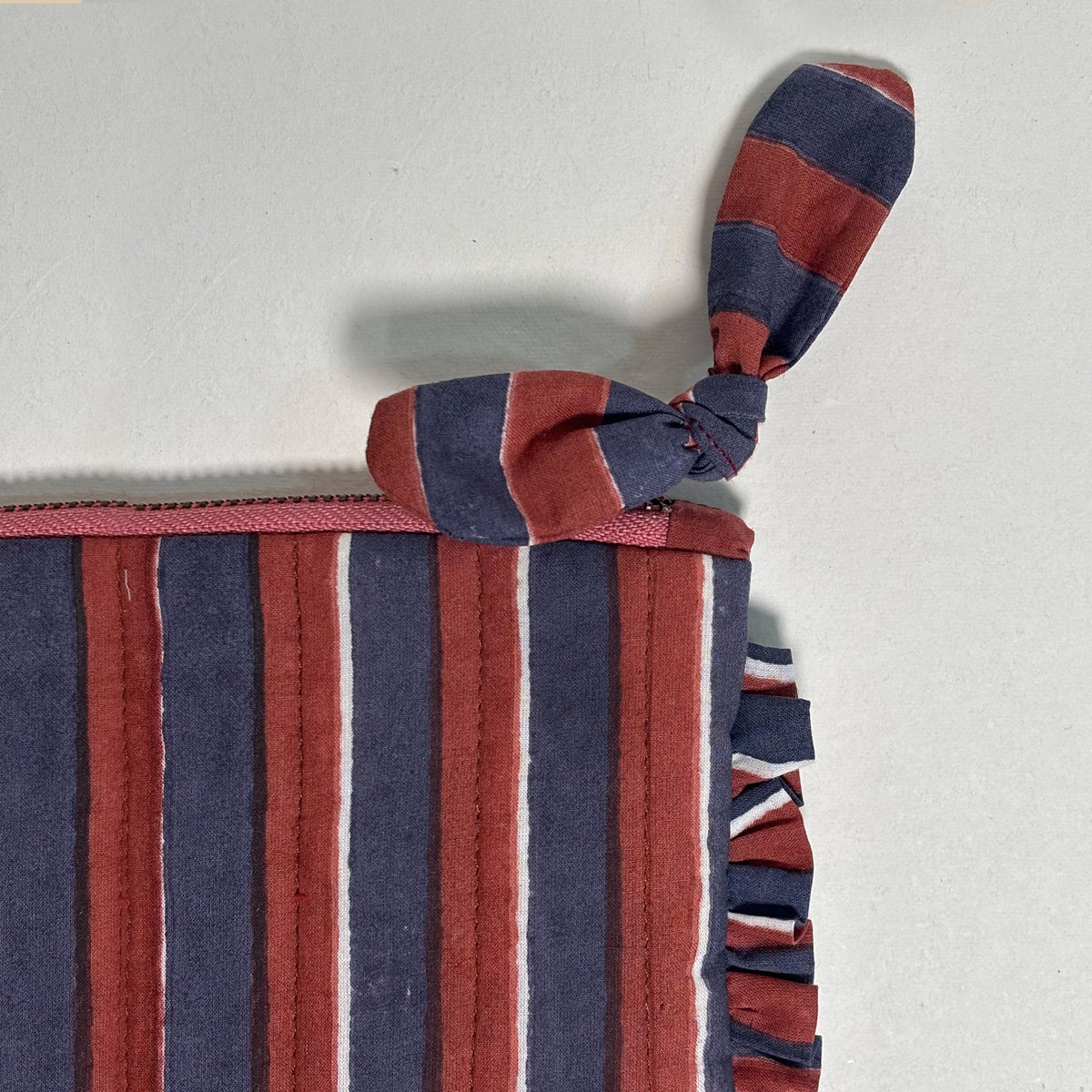 Striped quilted travel pouch with frill trim, bow tie handle, and zipper
