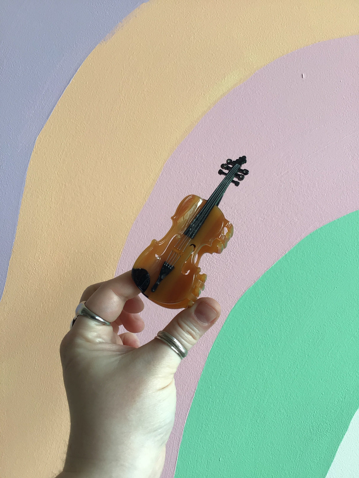 Musical hair claw shaped like a brown violin with black strings and gold accents