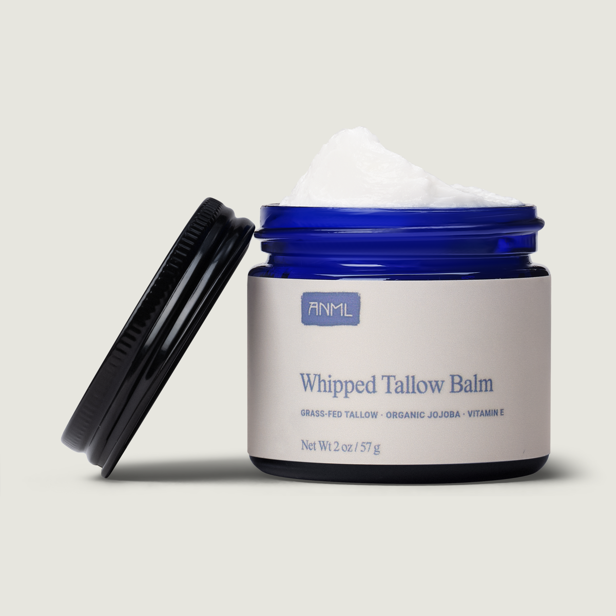 Whipped tallow balm jar with blue lid, topped with pale white whipped balm and spatula