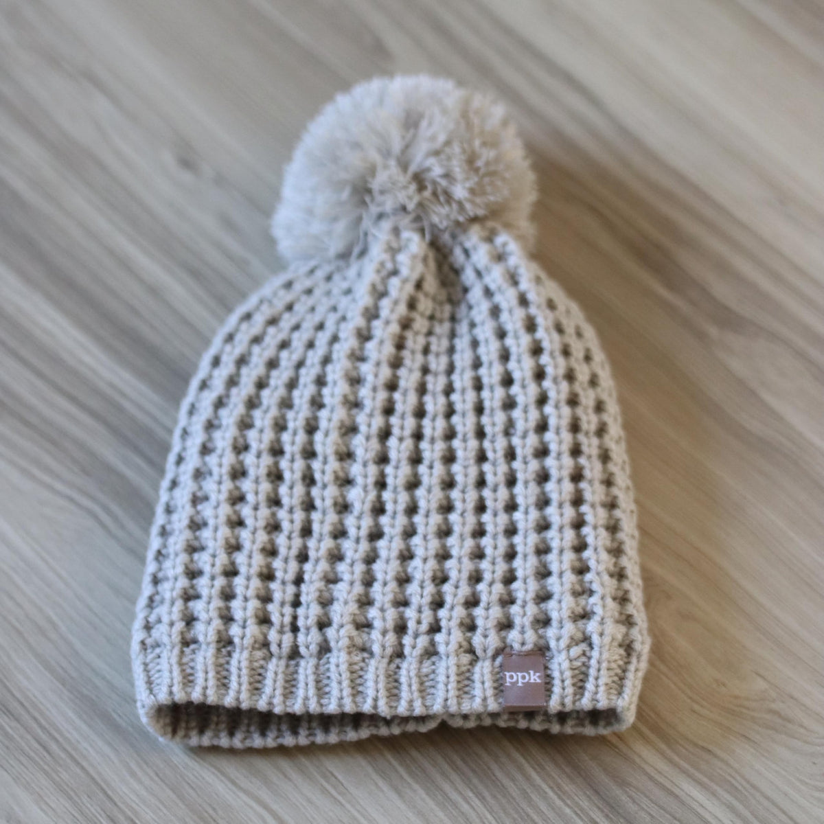 Beige knit beanie with pom-pom, ribbed cuff, and small brand label