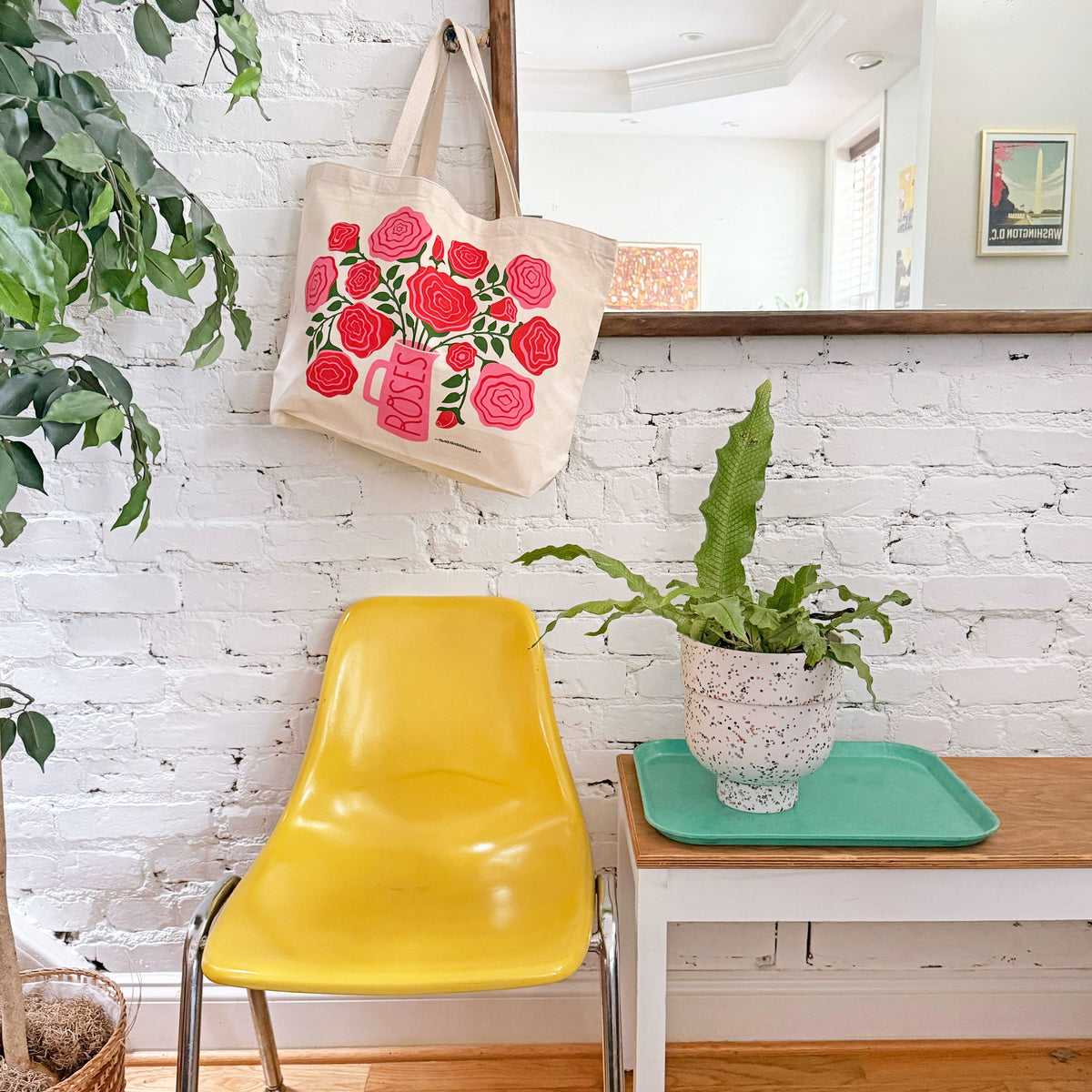 Off-white tote bag hanging by handles, with red and pink rose bouquet and pink vase print