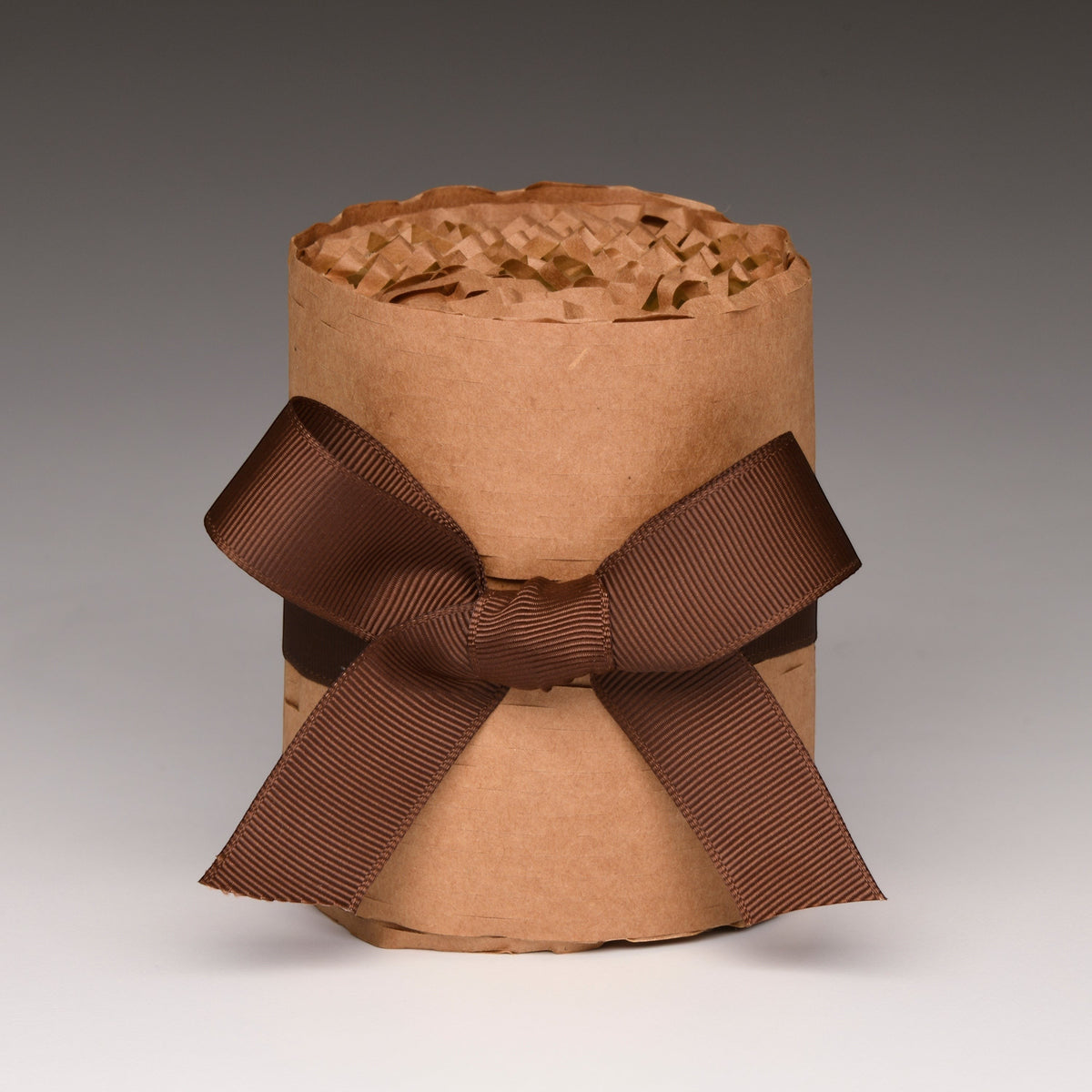 Kraft wrapped candle with brown ribbon bow, textured paper top and amber jar base