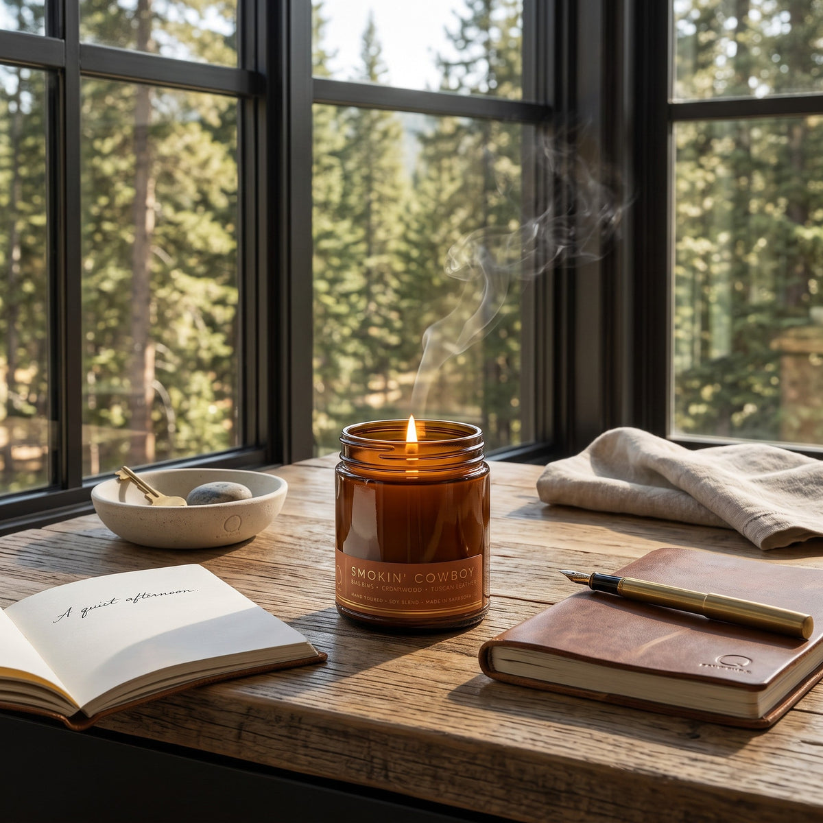 Amber soy candle in glass jar with lit wick, on wooden tabletop with nearby items.