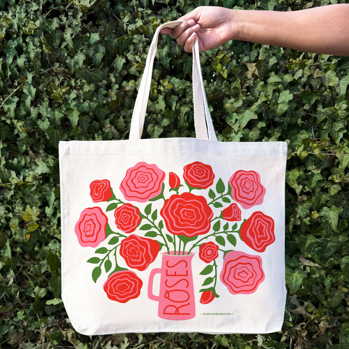 Off-white tote bag held up, showing red and pink rose bouquet and pink vase design