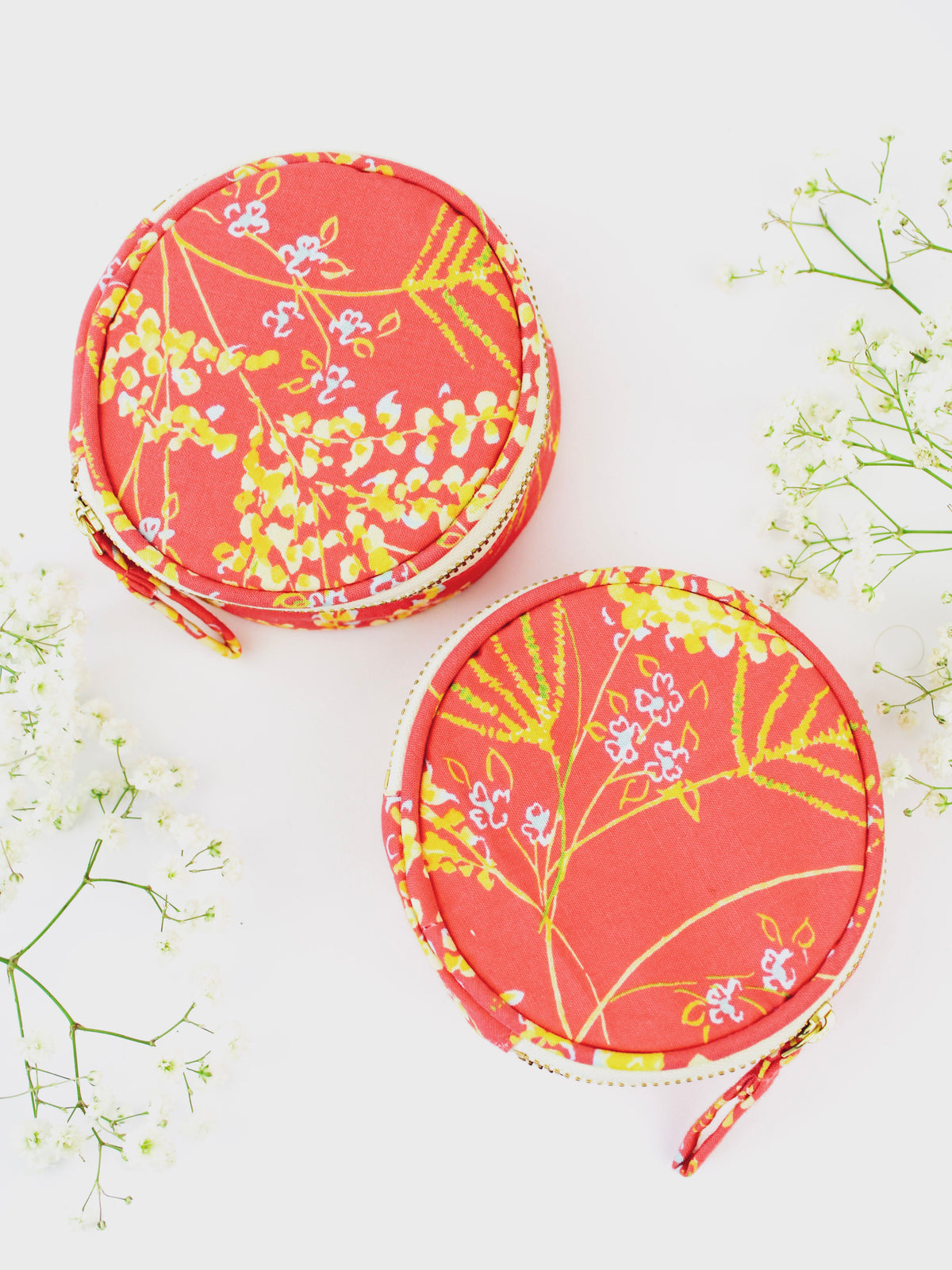 Two coral floral round jewelry pouches with gold zipper edges