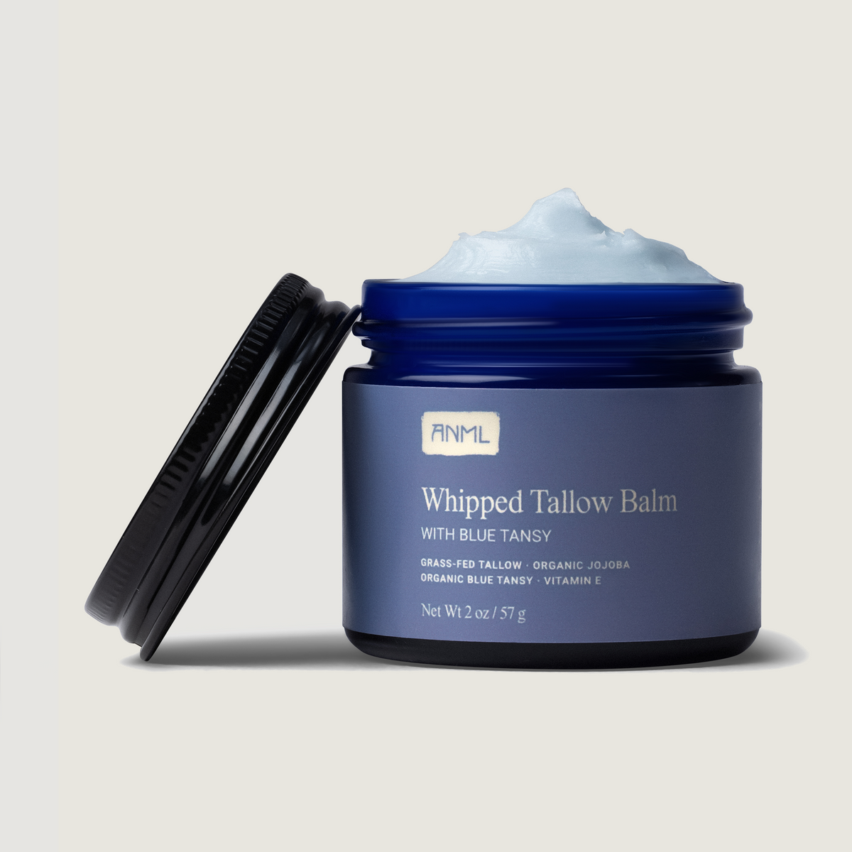 Whipped tallow balm jar with blue lid, holding visible pale blue cream and spatula