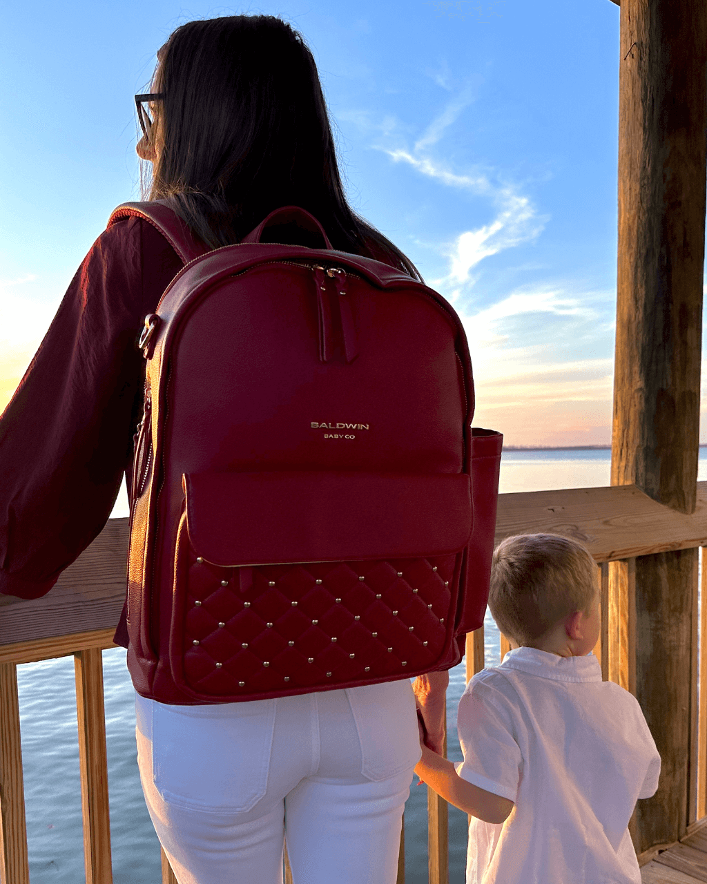 Crimson diaper backpack worn on the back, with a quilted front pocket.