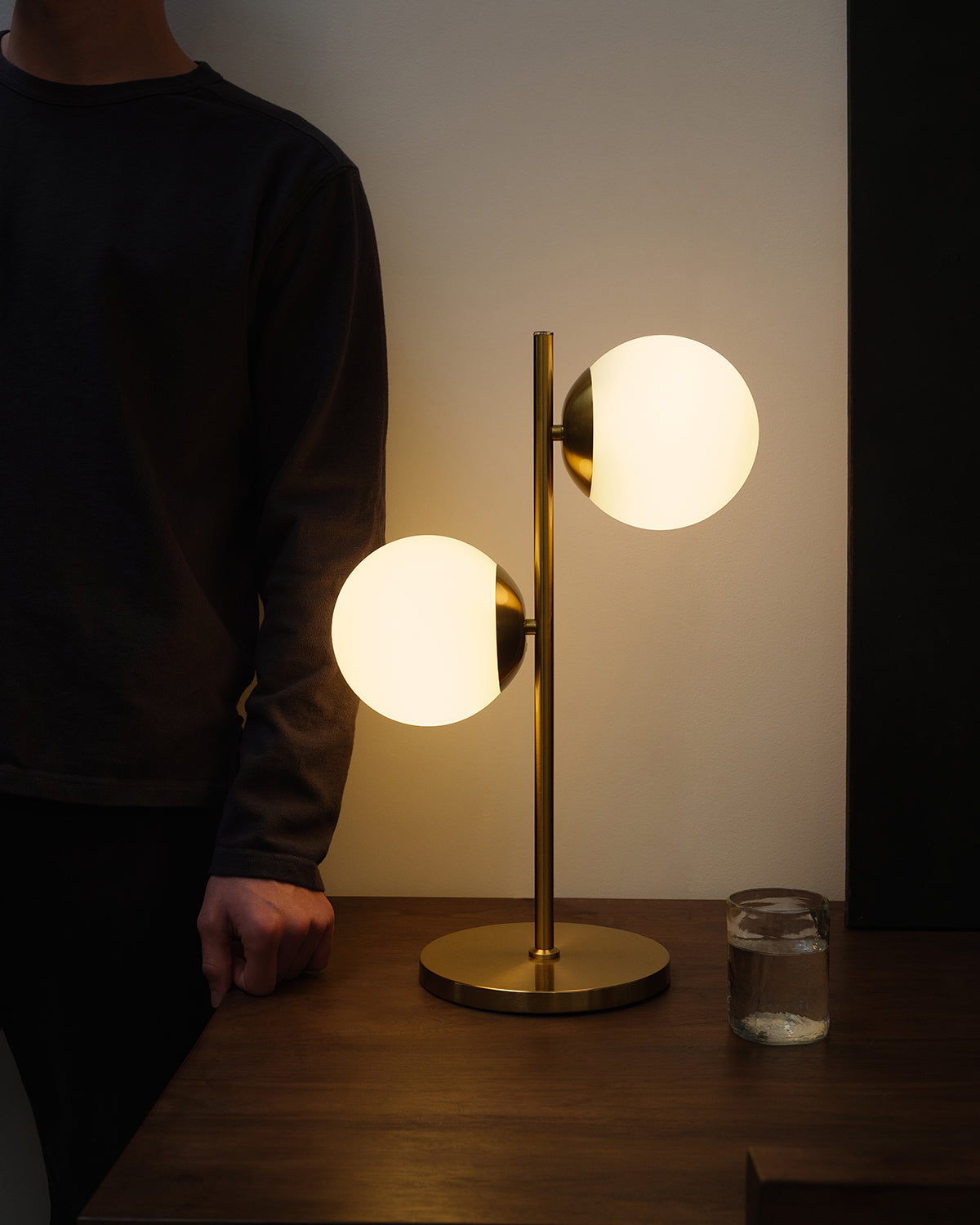 Two-globe table lamp with white shades and gold brass stand on wooden table