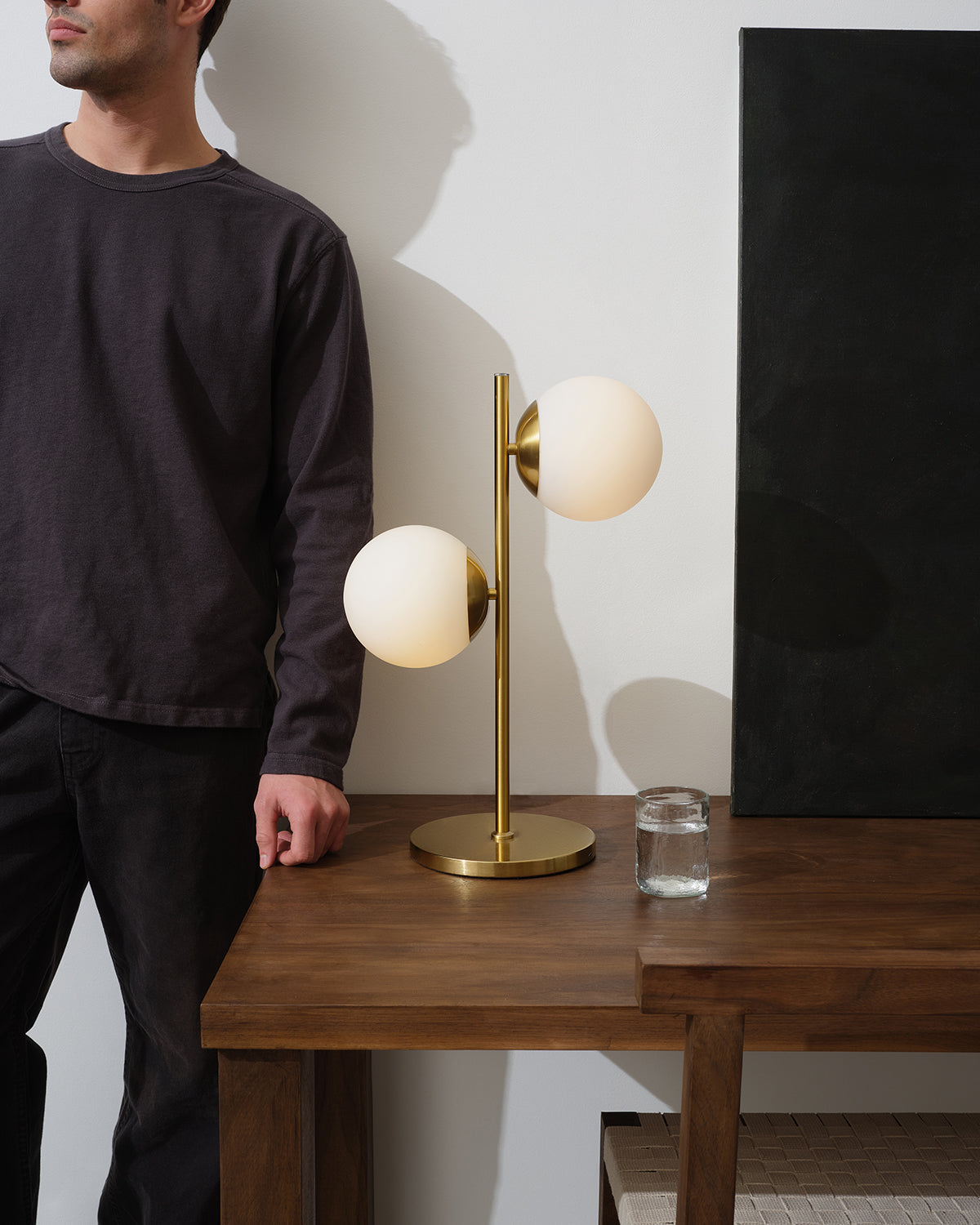 Two-globe table lamp with white shades on gold base, brass stem beside glass jar