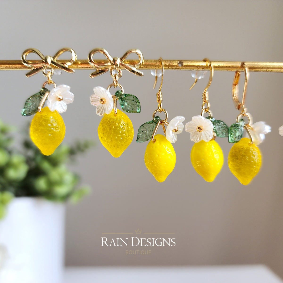 Assorted lemon dangle earrings on display bar: yellow charms, green leaves, white flower details