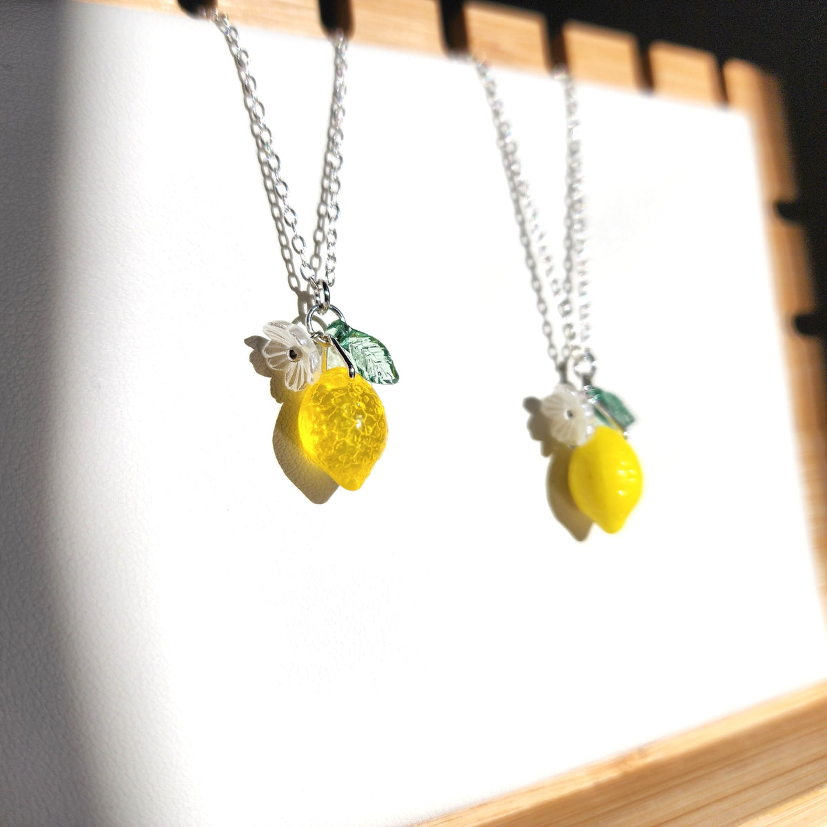 Two lemon pendant necklaces with yellow lemon charm, white flower, and green leaf