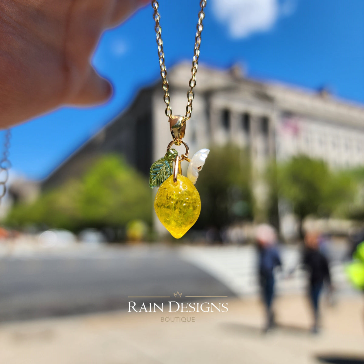 Gold chain lemon pendant necklace with yellow lemon charm, white flower, and green leaf